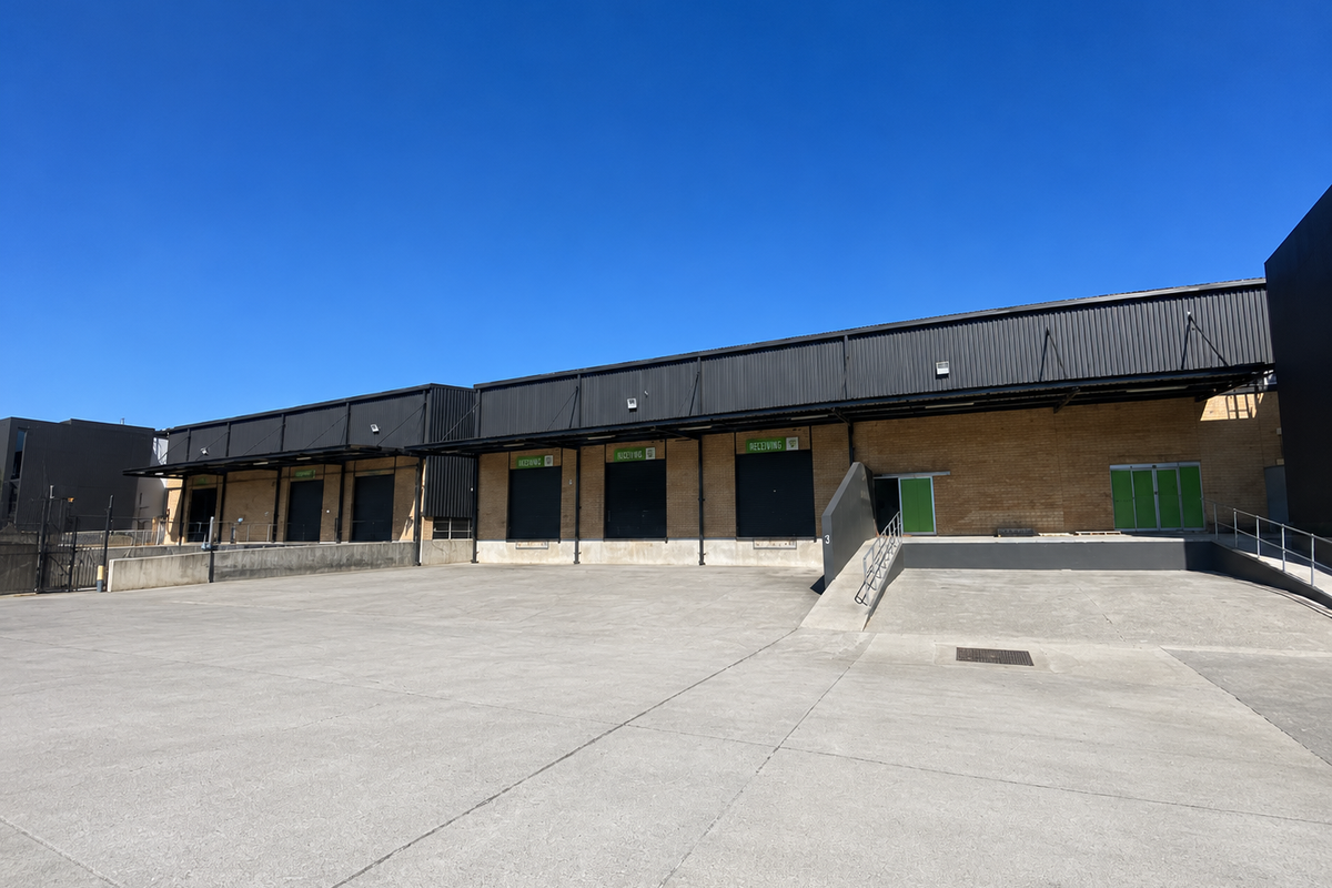 Industrial warehouse exterior featuring multiple loading docks with roller shutter doors and a spacious concrete yard area.