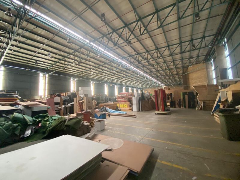 Large industrial warehouse space featuring high exposed steel truss ceilings, concrete flooring, and metal wall cladding, suitable for storage or manufacturing operations.