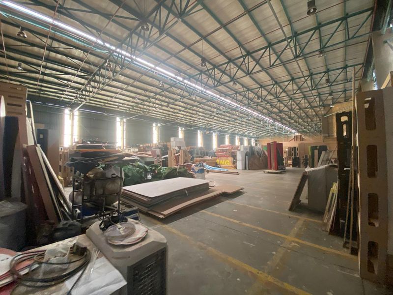 Spacious industrial warehouse featuring high exposed steel roof trusses, concrete flooring, and functional industrial lighting, suitable for storage or manufacturing operations.
