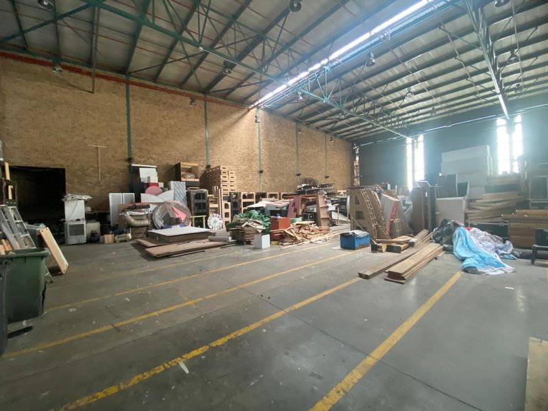 Spacious industrial warehouse unit featuring high exposed steel roof trusses, durable concrete flooring, and brick walls, suitable for storage or light manufacturing operations.