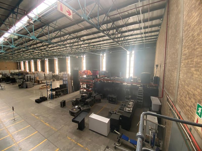 Spacious industrial warehouse featuring high ceilings with exposed steel trusses, concrete flooring, and natural light through skylights and side windows.