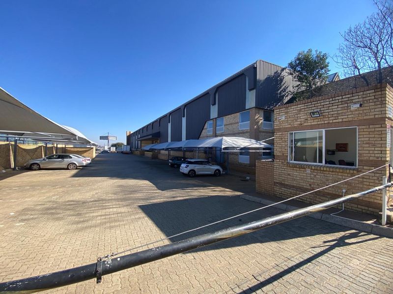 Industrial property exterior featuring a paved driveway, security guard house, and multiple shade cloth carports for parking.