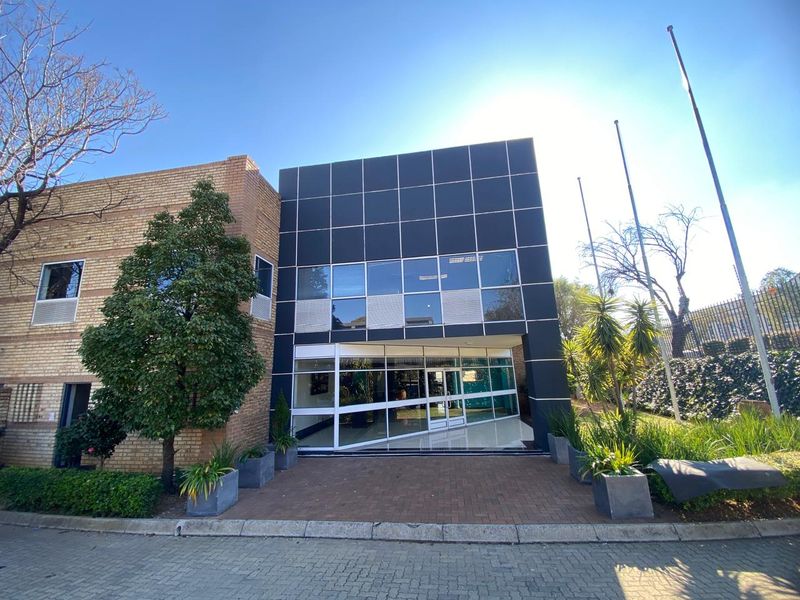 Front elevation of an industrial office building featuring a modern black panel facade, glass entrance, and paved approach.