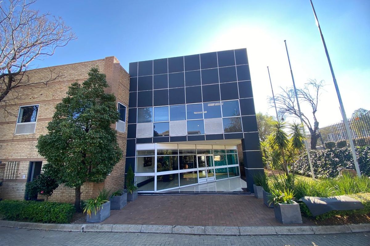 Front elevation of an industrial office building featuring a modern black panel facade, glass entrance, and paved approach.