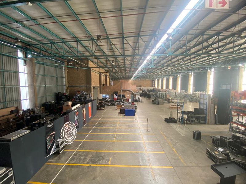 Spacious industrial warehouse featuring high ceilings with exposed steel trusses, concrete flooring, and ample natural light through skylights and side windows.