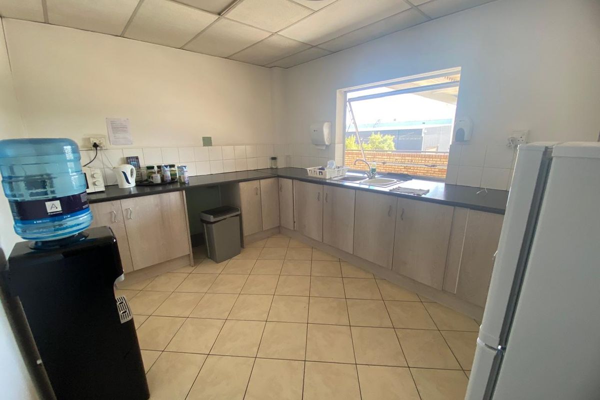 Functional industrial kitchen area featuring laminate cabinetry, tiled flooring, a stainless steel sink, and a drop ceiling with integrated lighting.