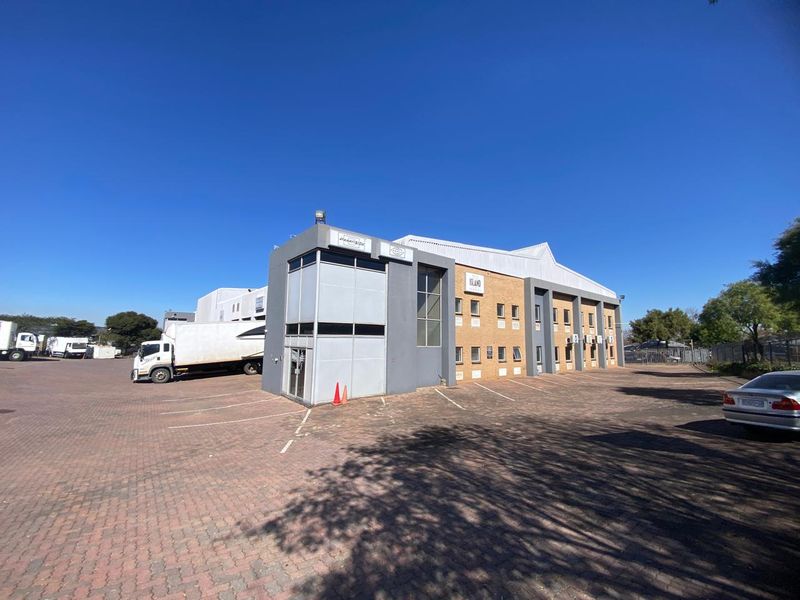 A wide-angle view of an industrial property featuring a multi-story brick and rendered facade with ample paved parking space and external air conditioning units.