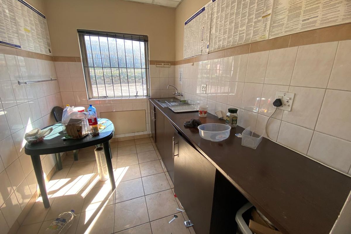 A functional industrial kitchen area featuring tiled walls, built-in cabinetry, a stainless steel sink, and security bars on the window.