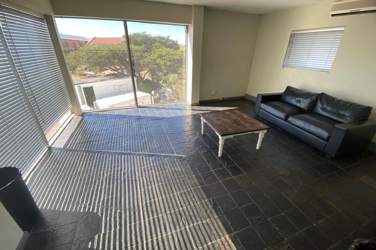 Spacious living area featuring dark slate tile flooring, large windows with venetian blinds, and a wall-mounted air conditioning unit.