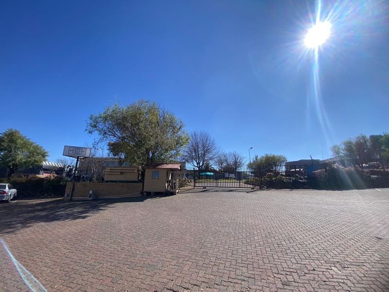 Front entrance view of the industrial property featuring a paved driveway, security gate, and guard booth.