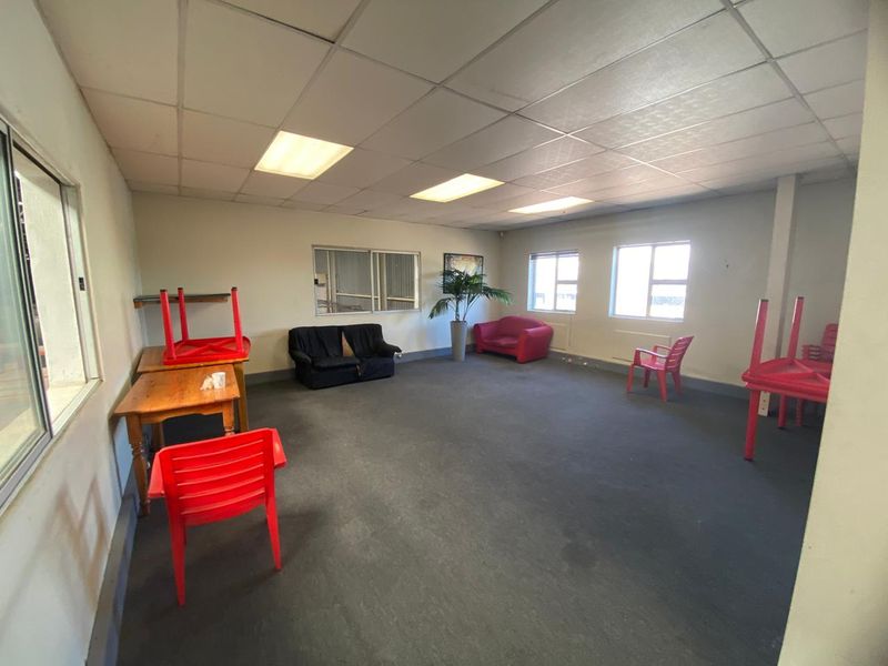 Spacious industrial office area featuring a suspended ceiling, recessed lighting, and carpeted flooring, offering a versatile workspace layout.
