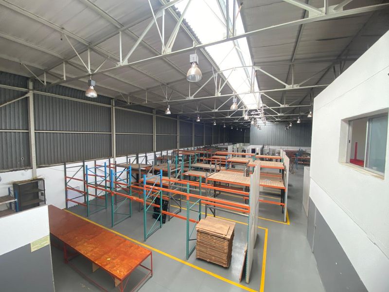 Spacious industrial warehouse area featuring high ceilings with exposed steel trusses, skylights, industrial lighting, and extensive built-in steel racking systems.