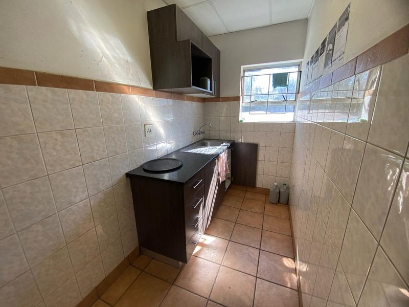 A compact scullery or utility area featuring tiled walls, built-in cabinetry with a stainless steel sink, and tiled flooring.