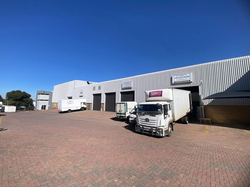 Industrial warehouse facility featuring corrugated metal cladding, multiple roller shutter access doors, and a spacious paved yard area for logistics and vehicle access.