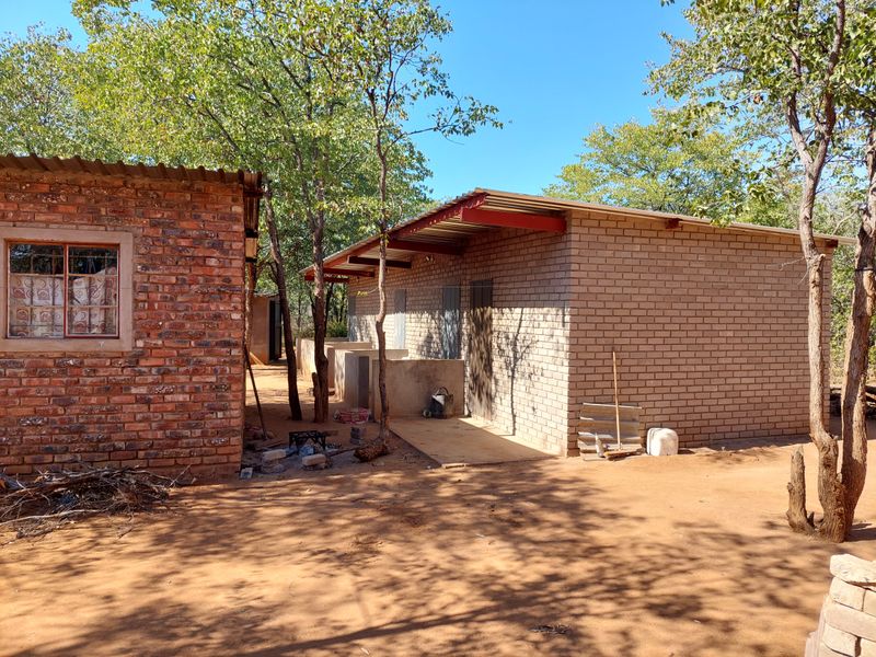 Exterior view of a rustic farm outbuilding featuring brick construction and a corrugated metal roof set within a natural wooded environment.