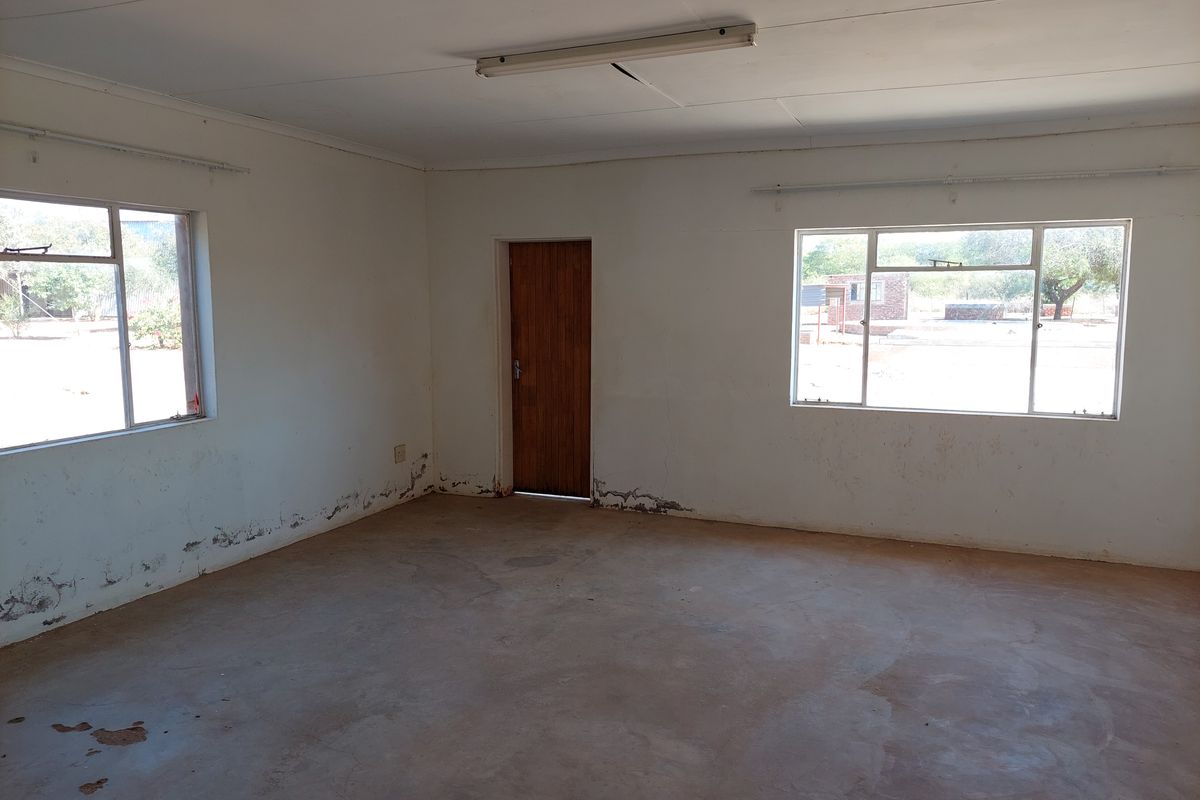 An empty, sunlit living area featuring concrete floors, aluminium windows, and a timber door, requiring cosmetic updates and repairs to the walls and ceiling.