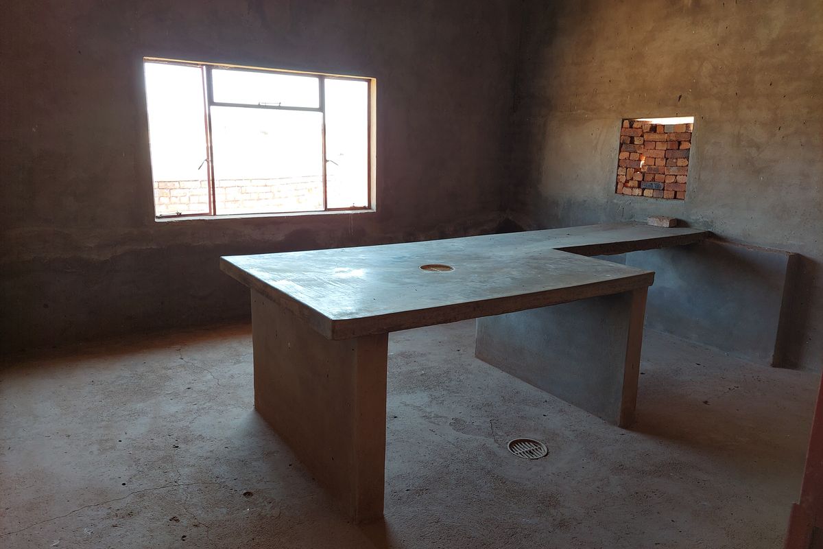 An unfinished kitchen space featuring a concrete island and countertop, with raw wall finishes and an exposed brick section.
