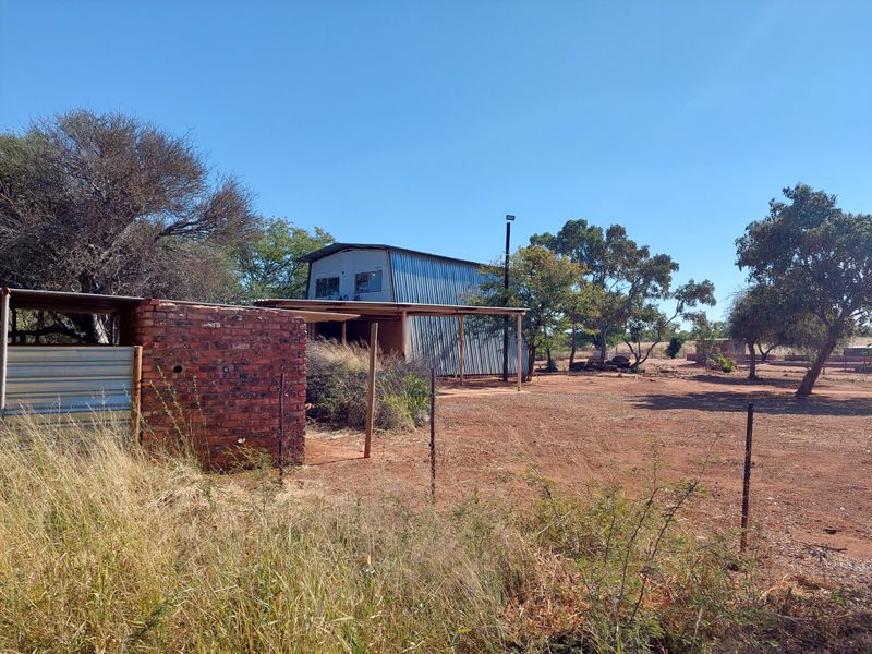 Rear view of the farm property featuring a corrugated metal shed and a brick outbuilding set within a large, open rural landscape.
