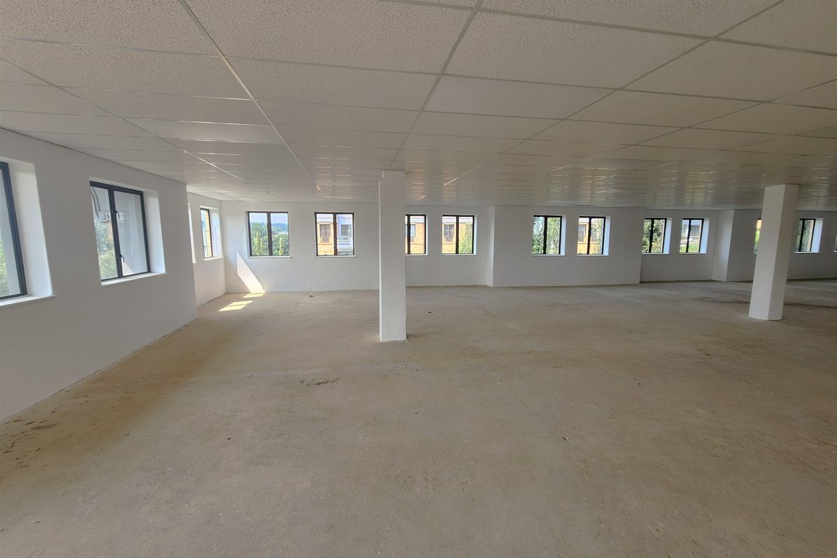 A large, open-plan office space featuring a suspended ceiling, structural columns, and multiple windows providing ample natural light, currently in shell condition.