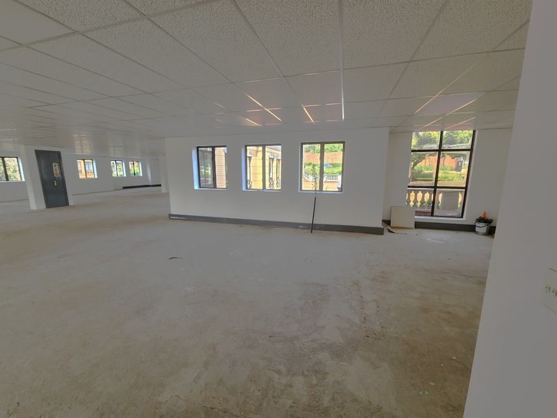 A large, open-plan office space featuring a suspended ceiling, recessed lighting, and expansive windows, currently in a shell condition awaiting final flooring finishes.