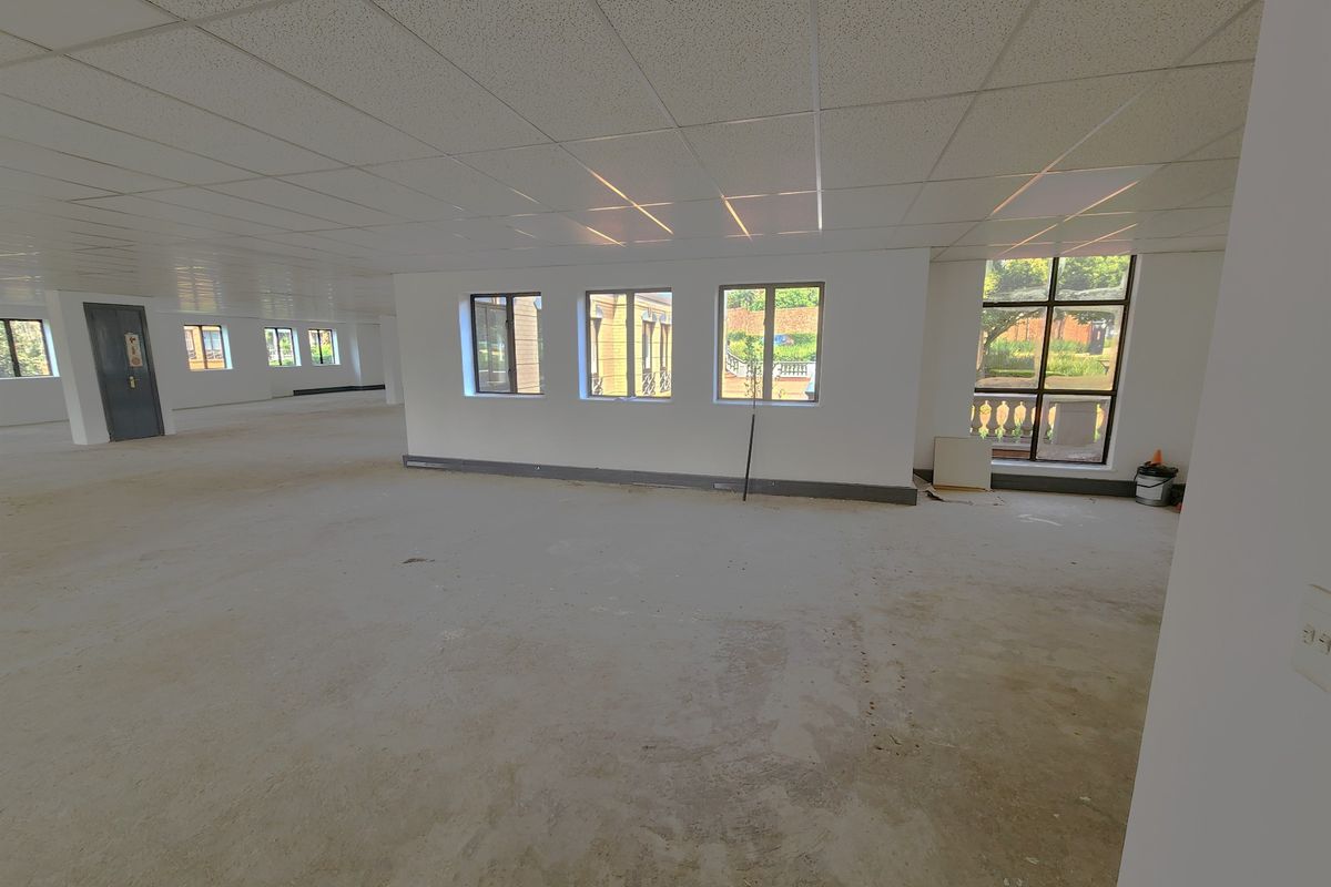 A large, open-plan office space featuring a suspended ceiling, recessed lighting, and expansive windows, currently in a shell condition awaiting final flooring finishes.