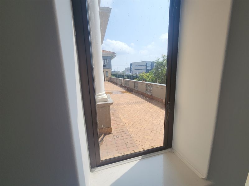 A view from an interior window looking out onto a paved balcony terrace featuring a balustrade and structural column.