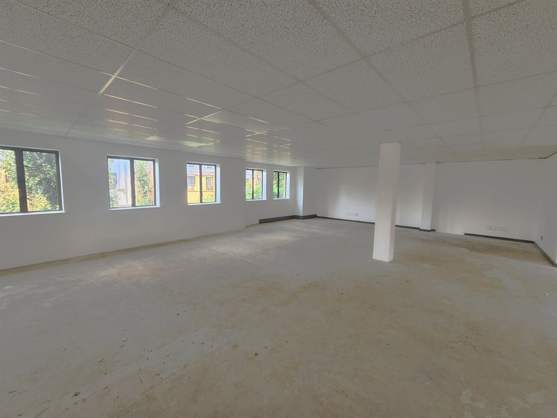 A spacious, open-plan office area featuring a suspended ceiling, structural support columns, and multiple windows providing natural light, currently in shell condition.