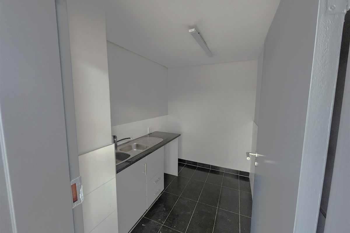 A compact office kitchenette featuring a stainless steel sink, laminate countertop, base cabinetry, and dark tiled flooring.