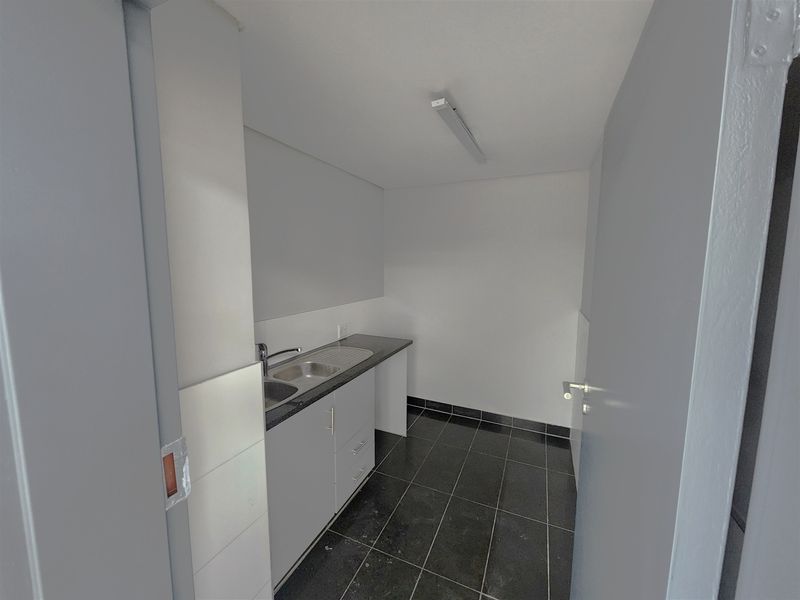 A compact office kitchenette featuring a stainless steel sink, laminate countertop, base cabinetry, and dark tiled flooring.