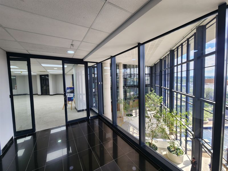 Modern office space featuring floor-to-ceiling glass walls, polished black tile flooring, and an open-plan layout with views into an internal atrium.