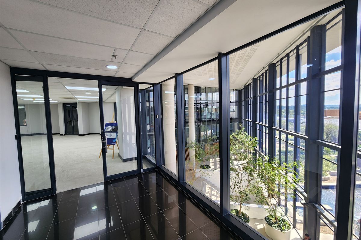 Modern office space featuring floor-to-ceiling glass walls, polished black tile flooring, and an open-plan layout with views into an internal atrium.