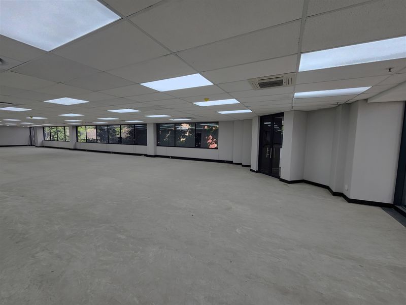 A spacious, open-plan office area featuring a suspended ceiling with recessed lighting, ducted air conditioning, and large windows providing ample natural light.