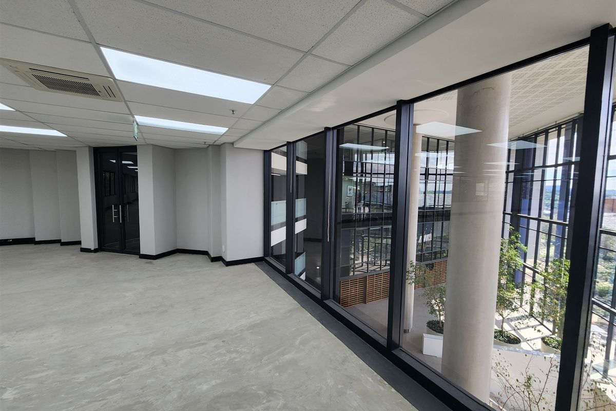 A modern, vacant office space featuring polished concrete floors, suspended ceilings with integrated lighting, and expansive glass partitioning overlooking an atrium.
