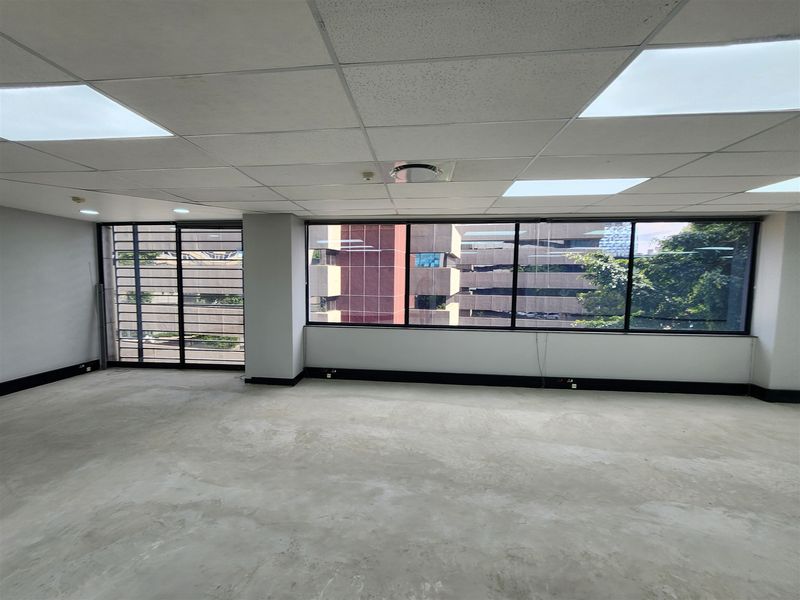 An empty, open-plan office space featuring a suspended ceiling, recessed lighting, and large windows with security bars, offering a blank canvas for customization.