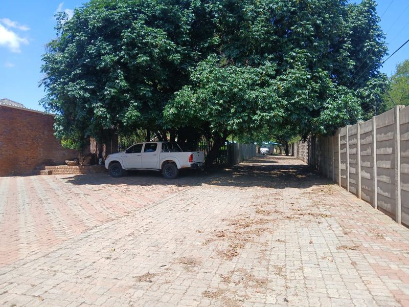A paved driveway area on a small holding featuring mature trees, a brick wall, and a precast concrete boundary wall.