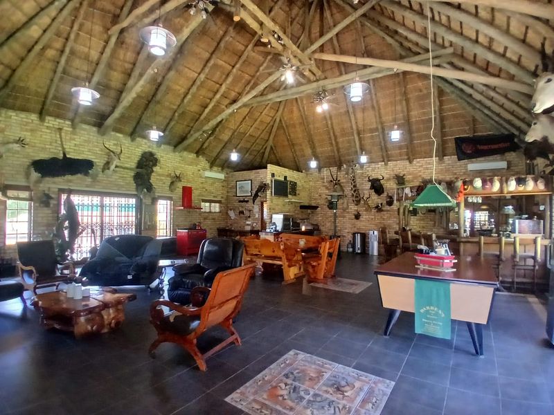 Spacious open-plan entertainment area featuring a high thatched roof with exposed timber trusses, exposed brick walls, tiled flooring, and a built-in bar.
