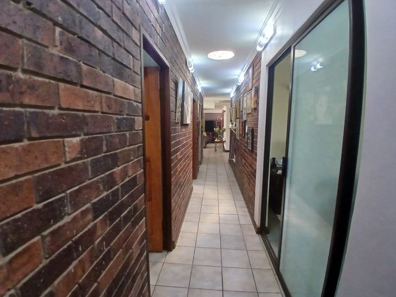 A long hallway featuring exposed brick walls, tiled flooring, and recessed lighting, providing access to multiple rooms within the property.