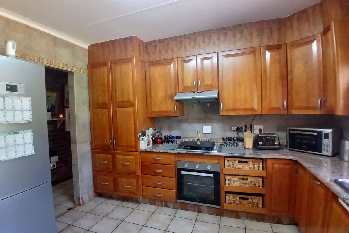 A functional kitchen featuring warm-toned wooden cabinetry, granite countertops, built-in oven, gas hob, and tiled flooring, offering ample storage and workspace.
