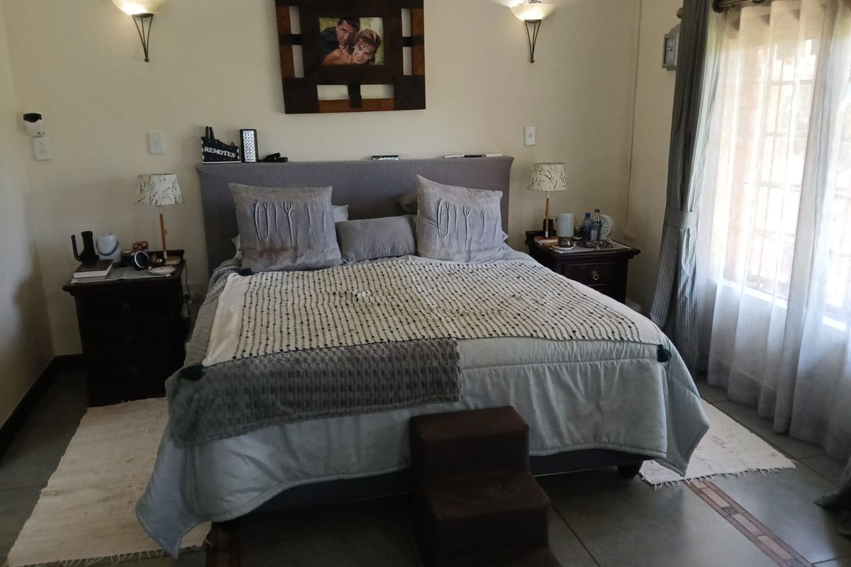A well-maintained bedroom featuring tiled flooring, wall-mounted lighting, and large windows with curtain rails, providing a comfortable and functional living space.
