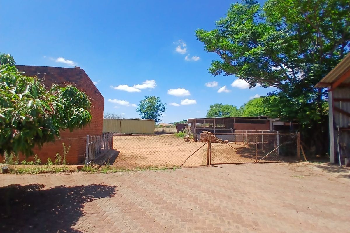 Rear exterior view of the small holding featuring brick paving, wire fencing, and various outbuildings on the property grounds.
