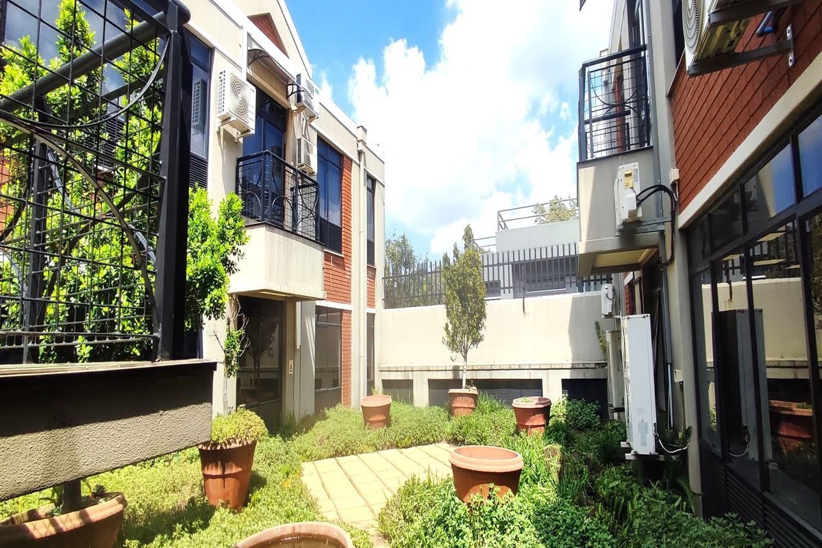 A rear courtyard area featuring a paved walkway, landscaped garden beds, and exterior building facades with mounted air conditioning units and balconies.