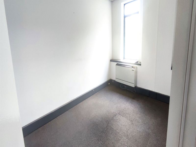 A vacant office space featuring carpeted flooring, a window for natural light, and a wall-mounted HVAC unit.