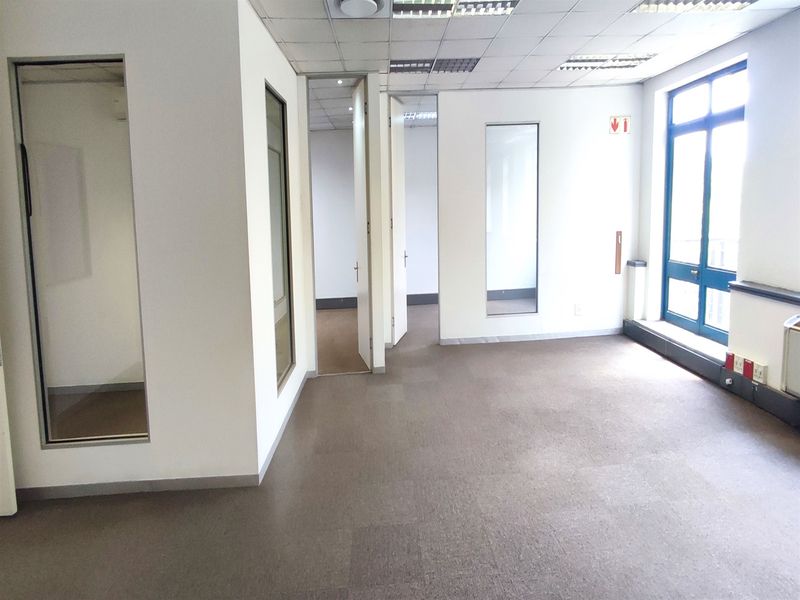 An empty, open-plan office space featuring carpeted flooring, suspended ceilings, and glass partition panels, offering a functional layout for professional use.