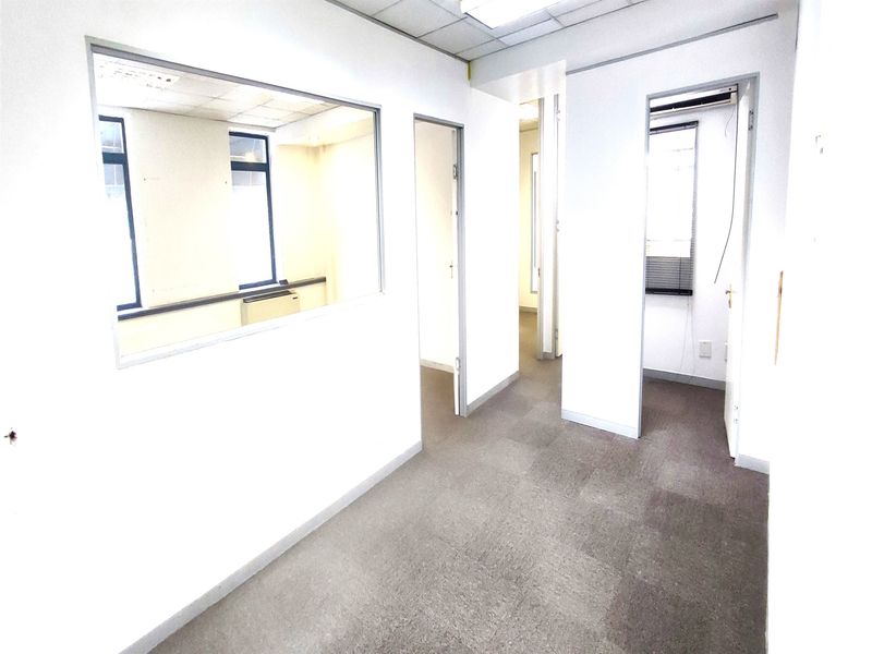 An empty office space featuring carpet tiles, a suspended ceiling, and an internal glass partition, offering a functional layout for professional use.
