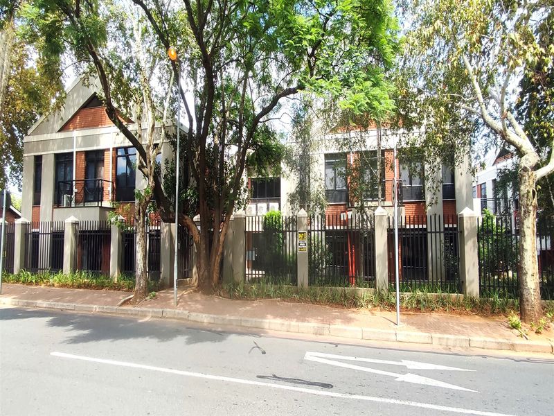 Front exterior view of a multi-story office building featuring brick masonry, metal security fencing, and a balcony, situated along a paved street.