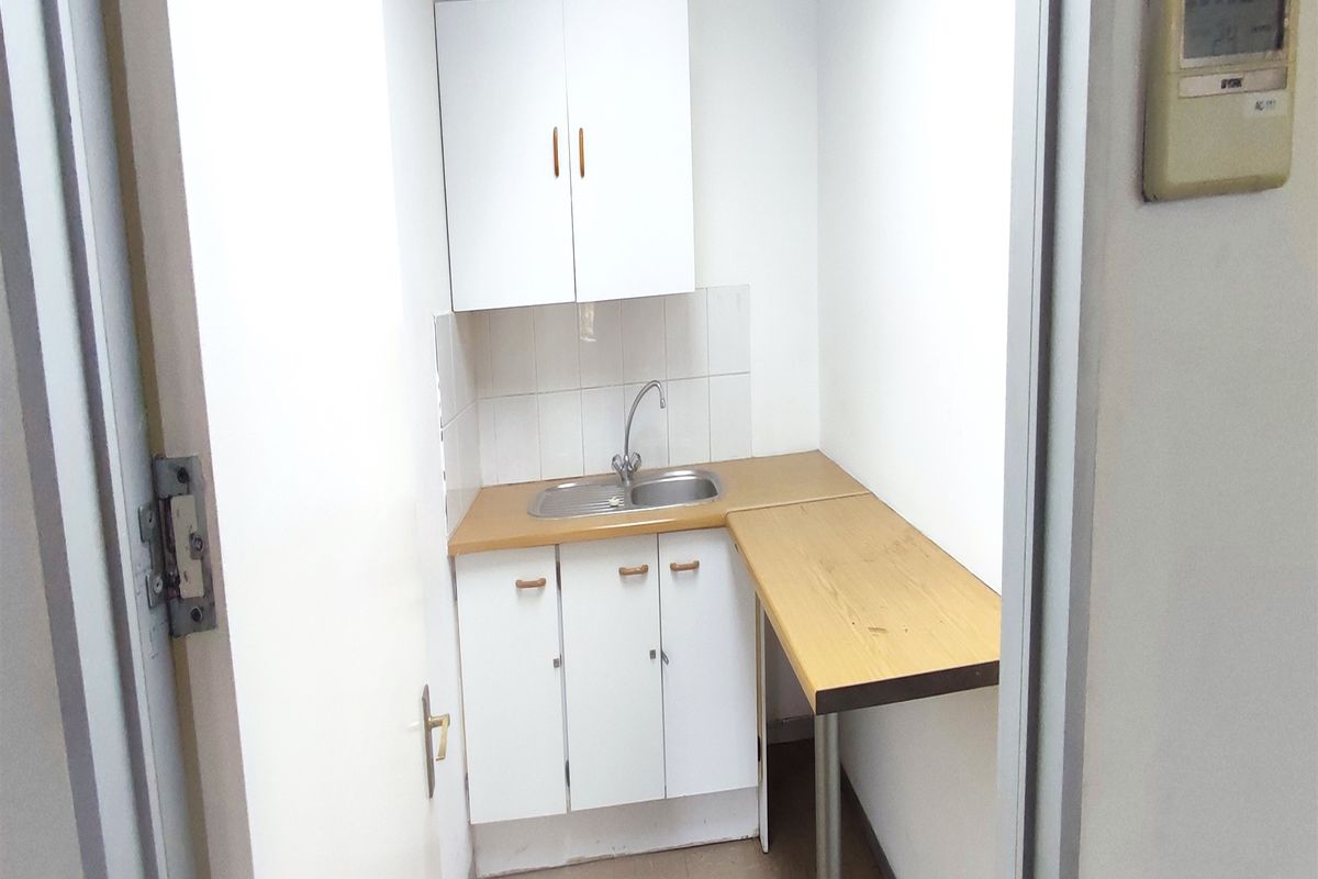 A compact kitchenette featuring built-in white cabinetry, a stainless steel sink, and a laminate countertop, suitable for a small office break area.