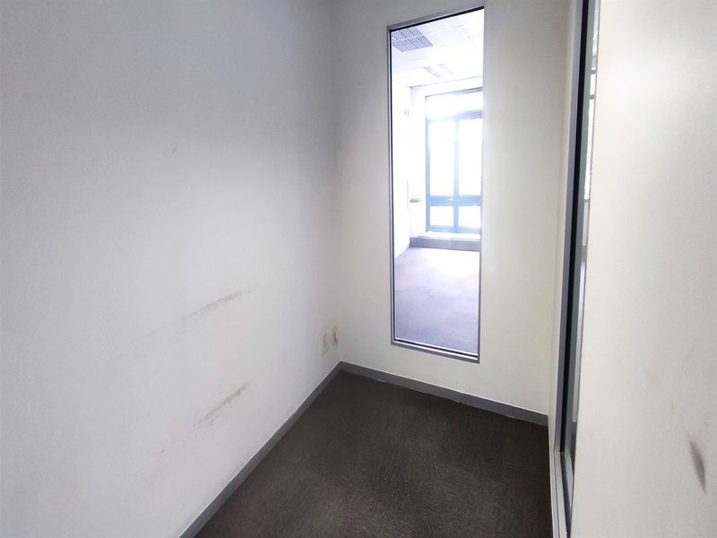 A small, empty office space featuring carpeted flooring and a glass partition wall, requiring minor cosmetic wall repairs.