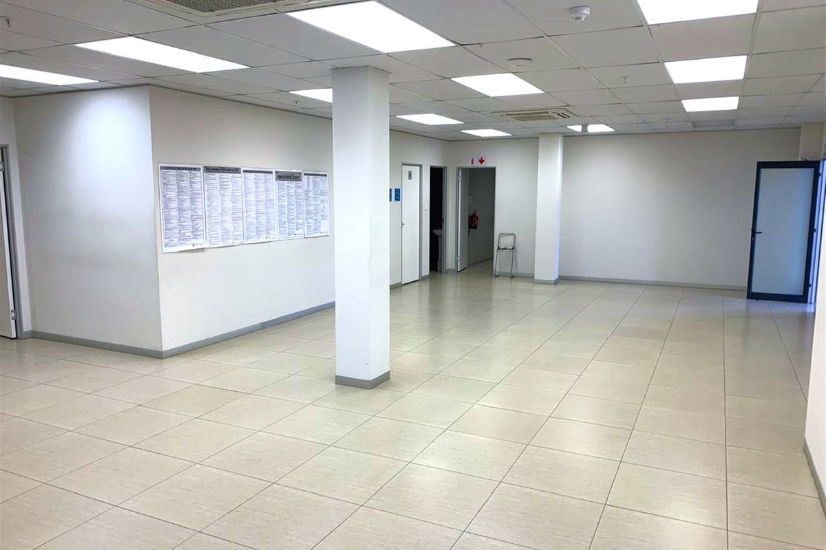 Spacious open-plan office area featuring neutral ceramic floor tiles, suspended ceiling with recessed lighting, and central air conditioning.
