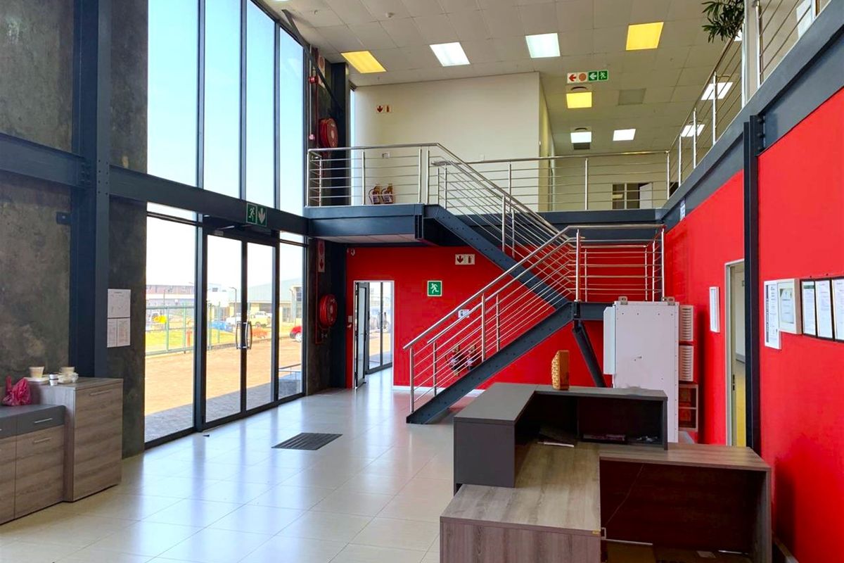 Spacious industrial entrance foyer featuring a mezzanine level, steel staircase with stainless steel balustrades, and expansive floor-to-ceiling windows providing ample natural light.