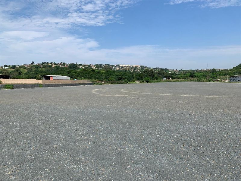 A large, level commercial land plot featuring a gravel surface and a retaining wall, offering expansive views of the surrounding landscape.